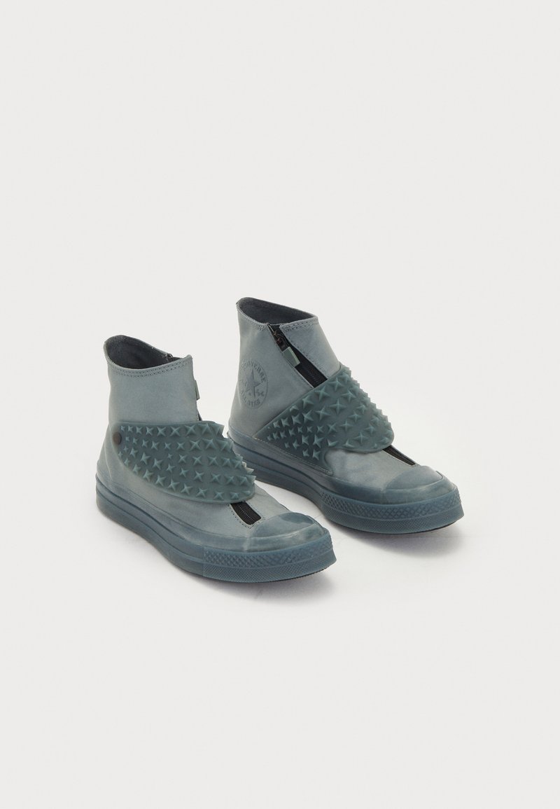 Tüübid kõrge varbaga spordijalatsid smaragdroheline kummist, millel on tähtkujuline nupud esirihmal, tõmbluku sulgemine ja tekstureeritud detailid, silmapaistva siledaga.