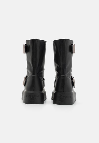 Bottes chelsea en cuir noir avec une finition légèrement brillante, doté d'une semelle épaisse et d'accents de boucle ajustables à l'arrière.