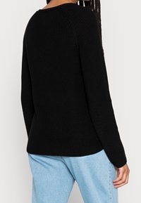 Suéter negro de punto con mangas largas, tejido texturizado, cuello redondo y detalles acanalados, combinado con jeans de color azul claro.