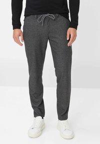 Grijze, gestructureerde joggingbroek met een elastische koordtaille. Heeft smalle pijpen en zijzakken, gecombineerd met witte sneakers.