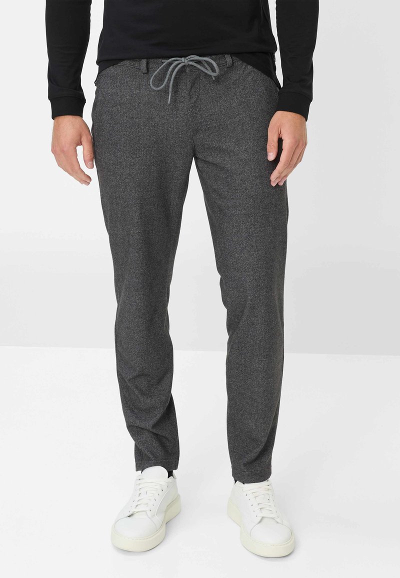 Grijze, gestructureerde joggingbroek met een elastische koordtaille. Heeft smalle pijpen en zijzakken, gecombineerd met witte sneakers.