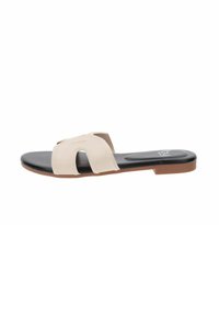 Sandalo scivoloso beige chiaro con una larga fascia superiore caratterizzata da dettagli intagliati, una soletta nera e una suola piatta con una base marrone.