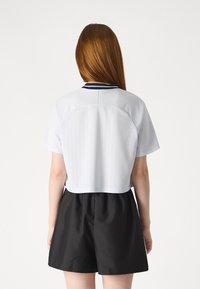 White short-sleeve cropped shirt with vertical stripes, navy collar, and a relaxed fit. Paired with black high-waisted shorts.