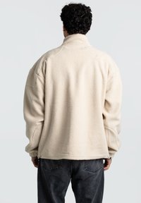 Pullover in pile color crema con colletto alto, vestibilità ampia e tessuto testurizzato. Presenta maniche arricciate e orlo dritto.