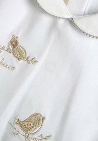 Indumento bianco con colletto rotondo, caratterizzato da ricami dorati di uccelli e fogliame. Tessuto morbido, impreziosito da piccoli dettagli di perline.