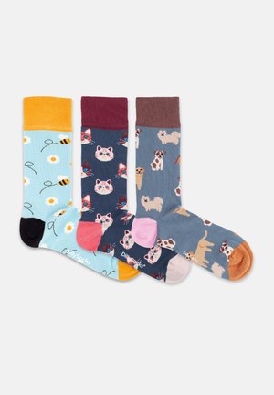 Tre farverige mønstrede sokker, én med bier og blomster, én med katteansigter og én med forskellige hundeillustrationer, alle med kontrasterende hæle og kanter.