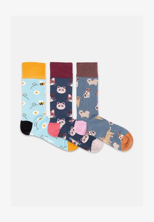 Tre farverige mønstrede sokker, én med bier og blomster, én med katteansigter og én med forskellige hundeillustrationer, alle med kontrasterende hæle og kanter.