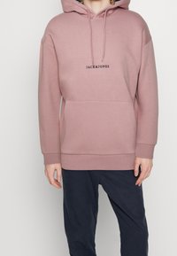 Roze hoodie van zacht materiaal, met een kangoeroezak en de tekst "JACK&JONES" in het zwart over de borst.