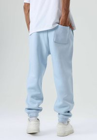 Lichtblauwe joggingbroek met elastische manchetten, een achterzak en een relaxte pasvorm, gecombineerd met witte schoenen en een eenvoudig wit shirt.