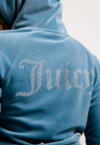 Plavi velur dukserica s kapuljačom, na leđima s natpisom "Juicy" od rhinestones. Glatka tekstura i uski dizajn.