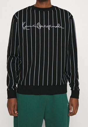 Sweatshirt noir avec des rayures blanches verticales, arborant un logo en écriture blanche sur la poitrine. Poignets et ourlet côtelés, texture douce.