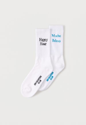 Dvoje bijelih čarapa za posadu s rebrastim rubovima, jedna izvezena s natpisom "Happy Hour" u crnoj boji, druga s natpisom "Mucho Relaxo" u plavoj boji.