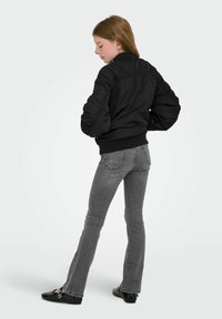 Črna podložena bomber jakna z rebrastim robom, napihnjenimi rokavi in gladko teksturo, kombinirana s temno sivimi razširjenimi kavbojkami in črnimi balerinkami.