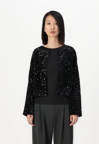 Giacca nera in paillettes con maniche lunghe, design corto e scollatura rotonda, abbinata a una maglietta nera e pantaloni grigi. Texture liscia, dettagli scintillanti.