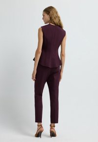 Top peplum imbottito e pantaloni sartoriali in un ricco bordeaux, caratterizzati da un design aderente, linee eleganti e dettagli minimali, abbinati a tacchi con cinturino.
