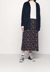 Marinblå kordjacka över en vit stickad tröja, i kombination med en midilång marinblå blommönstrad kjol och svarta högstövlar.