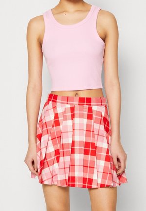 Femme portant un crop top rose sans manches et une jupe plissée à carreaux rouge et rose, montrée des épaules jusqu’à la mi-cuisse.