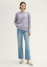 Paarse gebreide trui met een bootnek, gecombineerd met lichtblauwe flare jeans. Het model draagt beige platformschoenen. Eenvoudig ontwerp, gladde textuur.