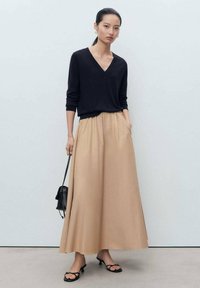 Sort v-hals sweater, let beige maxi nederdel med lommer og sort håndtaske. Glat stof, flade sandaler med en sløjfedetalje.