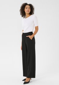 Weißes, enges Oberteil mit kurzen Ärmeln, kombiniert mit schwarzen weit geschnittenen Hosen mit elastischem Bund und seitlichen Taschen. Schwarze Absätze runden das Outfit ab.
