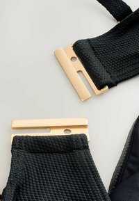 Svarta texturerade remmar med guldspännen, med rektangulär form och utskärningaccents. Slät tyg kompletterar designen.