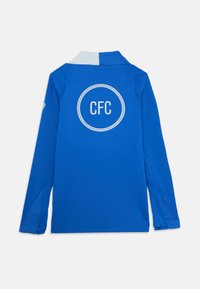 Hosszú ujjú kék pólóing világoskék gallérral. A hátsó részén fehér "CFC" logó található. Sima szövet textúra.