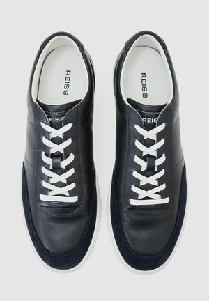 Tmavě modré kožené tenisky s bílými tkaničkami, hladkým svrškem a texturovaným semišovým detailem na špičce. Bílá gumová podrážka. Viditelné značení značky.