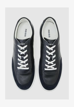 Tmavě modré kožené tenisky s bílými tkaničkami, hladkým svrškem a texturovaným semišovým detailem na špičce. Bílá gumová podrážka. Viditelné značení značky.