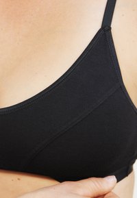Zwarte beha met verstelbare bandjes, zachte stof, naaddetails en een driehoekige vorm. Soepele textuur en eenvoudig ontwerp voor comfort.