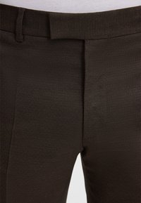 Braune, fein strukturierte Hose mit glatter Oberfläche, ausgestattet mit flacher Vorderseite, Gürtelschlaufen und maßgeschneiderter Passform. Keine sichtbaren Beschläge oder Muster.