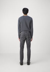 Grå långärmad skjorta och grå jeans med slim fit. Jeansen har två bakfickor med kurviga stickningsdetaljer.