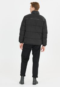 Sort puffet jakke med høj krave, horisontalt quiltet mønster og elastiske manchetter, båret med sorte bukser og ankelstøvler.