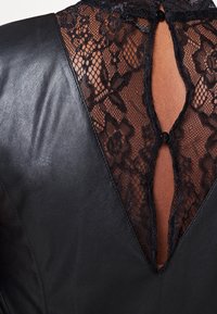 Schwarzes Lederoberteil mit einem Spitzenrücken, der florale Muster zeigt, V-Ausschnitt-Design und einem Knopfverschluss hinten. Sanfte Textur.
