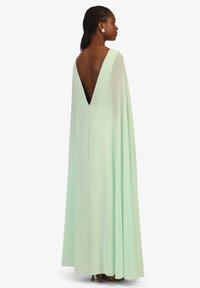 Robe longue vert menthe avec un décolleté en V profond, en tissu fluide et à la silhouette ample. Présente de grandes boucles d'oreilles rondes.