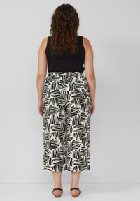Zwarte tanktop met hoge taille, wijde broek met een zwart-wit bladerenpatroon en een elastische tailleband. Platte sandalen.