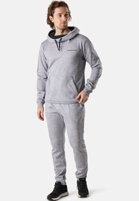 Hellgrau Hoodie und passende Jogginghose aus strukturiertem Stoff mit einer Vordertasche, Kapuze mit Kordelzug und Logo-Detail auf der Brust.