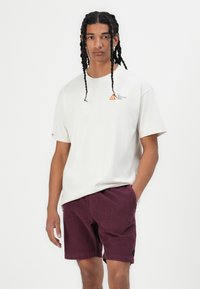 Crème korte mouwen t-shirt met een klein oranje driehoeklogo, gecombineerd met bordeaux corduroy shorts met een zijlogo patch.