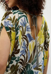 Bluse med blomstermønster i forskellige farver, med en dyb V-udskæring bagpå og en knytelukning, korte ærmer og et let, struktureret stof.