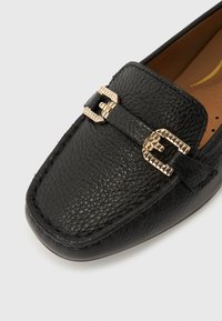 Mocasini negri din piele texturată, cu catarame decorative aurii în față și interior căptușit maro.