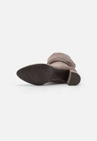 Bota de ante taupe para mujer de media caña tumbada de lado, mostrando la suela texturada y el tacón cuadrado sobre un fondo blanco.