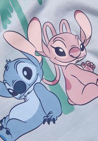 Cartoonfiguren op een lichtblauwe stof: een figuur is blauw met een ronde lichaam, de andere is roze met grote oren, beide glimlachend.