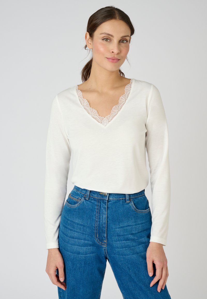 Witte langemouwen top met een V-hals en delicate kanten afwerking. Gecombineerd met hoog getailleerde donkerblauwe jeans met een gestructureerd patroon.