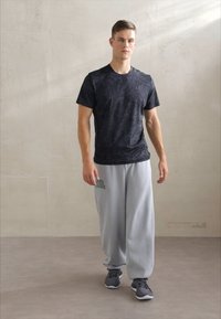 Černé texturované sportovní tričko, kombinované se šedými tepláky s zeleným potiskem. Model má na sobě šedé tenisky. Jednoduchý, moderní neformální outfit.