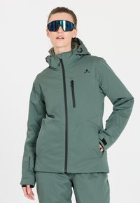 Grüne isolierte Jacke mit Kapuze, ausgestattet mit einer mit Reißverschluss versehenen Brusttasche und schwarzen Akzenten. Hergestellt aus strukturiertem Stoff, geeignet für den Outdoor-Einsatz.