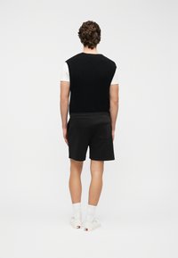 Μαύρο πλεκτό γιλέκο πάνω από ένα λευκό μπλουζάκι, συνδυασμένο με μαύρο σορτς. Απλός σχεδιασμός, άνετη εφαρμογή και λευκά αθλητικά παπούτσια με πολύχρωμες λεπτομέρειες.