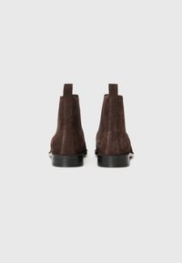 Botas Chelsea de ante marrón oscuro con una textura suave, paneles laterales elásticos y un tacón bajo de goma negra. Diseño limpio y minimalista.