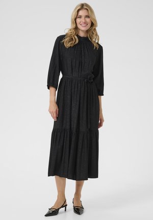 Robe noire midi avec un corsage plissé, des manches trois quarts et une taille nouée. Présente un ourlet à volants superposés et une texture scintillante.