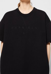 Camiseta negra de gran tamaño hecha de algodón. Cuenta con un cuello redondo acanalado, mangas cortas y un logo bordado "MARGIELA 6" en la parte frontal.