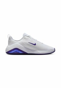 Zapatillas deportivas blancas con un upper texturizado, símbolo de Nike en púrpura y una unidad de amortiguación con tinte púrpura en el talón. Suela de goma para mayor tracción.