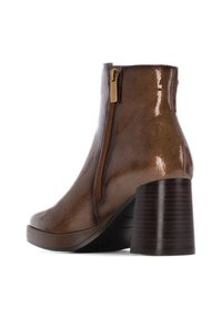 Botín de tobillo de charol marrón con cremallera lateral, punta redonda y un tacón grueso y estriado de madera oscura. Textura suave con un acabado brillante.